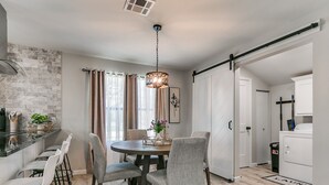Una cocina moderna con salpicadero de piedra, un comedor con mesa y sillas redondas, y una puerta corredera que da a un cuarto de lavado.