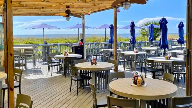 An outdoor patio area with round tables and chairs, umbrellas, and a view of the ocean. - Modern & Sleek condo Beachfront Resort HHI for 6, private balcony & beach access (Hilton Head Island)