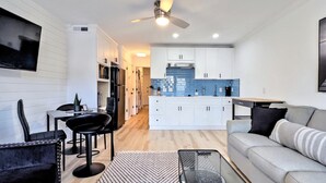 A modern living room with a sofa, a coffee table, and a TV. There is a kitchen in the background with white cabinets and a blue backsplash. - Modern & Sleek condo Beachfront Resort HHI for 6, private balcony & beach access (Hilton Head Island)