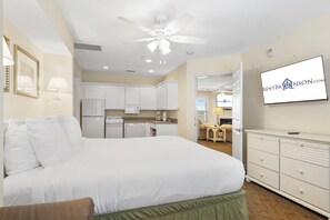A hotel room with a bed, a television, a kitchenette, and a ceiling fan.