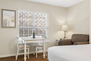 A hotel room with a bed, a desk with two chairs, a lamp, and a window with blinds.