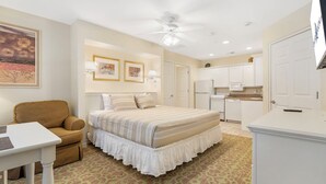 Une chambre comprenant un lit, un bureau, une chaise, un ventilateur de plafond et un coin cuisine.