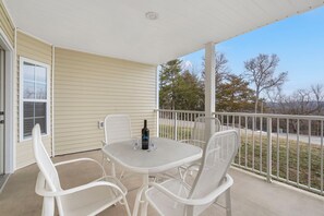 A covered patio with a table and chairs, a bottle, and glasses. - Roomy Condo with Tranquil Views, Lake Access, Outdoor Pool & Free Attraction Tickets (Kimberling City)