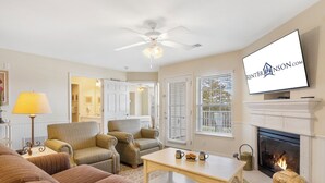 A living room with a fireplace, a television mounted above it, and a ceiling fan. - Roomy Condo with Tranquil Views, Lake Access, Outdoor Pool & Free Attraction Tickets (Kimberling City)