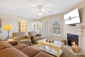 Un salon avec une cheminée, un téléviseur et un ventilateur de plafond.