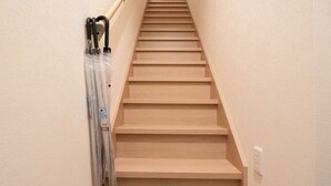 A wooden staircase with a handrail on the left, a pair of slippers on the floor, and a suitcase on the right. - HANASTAY OKA (Osaka)