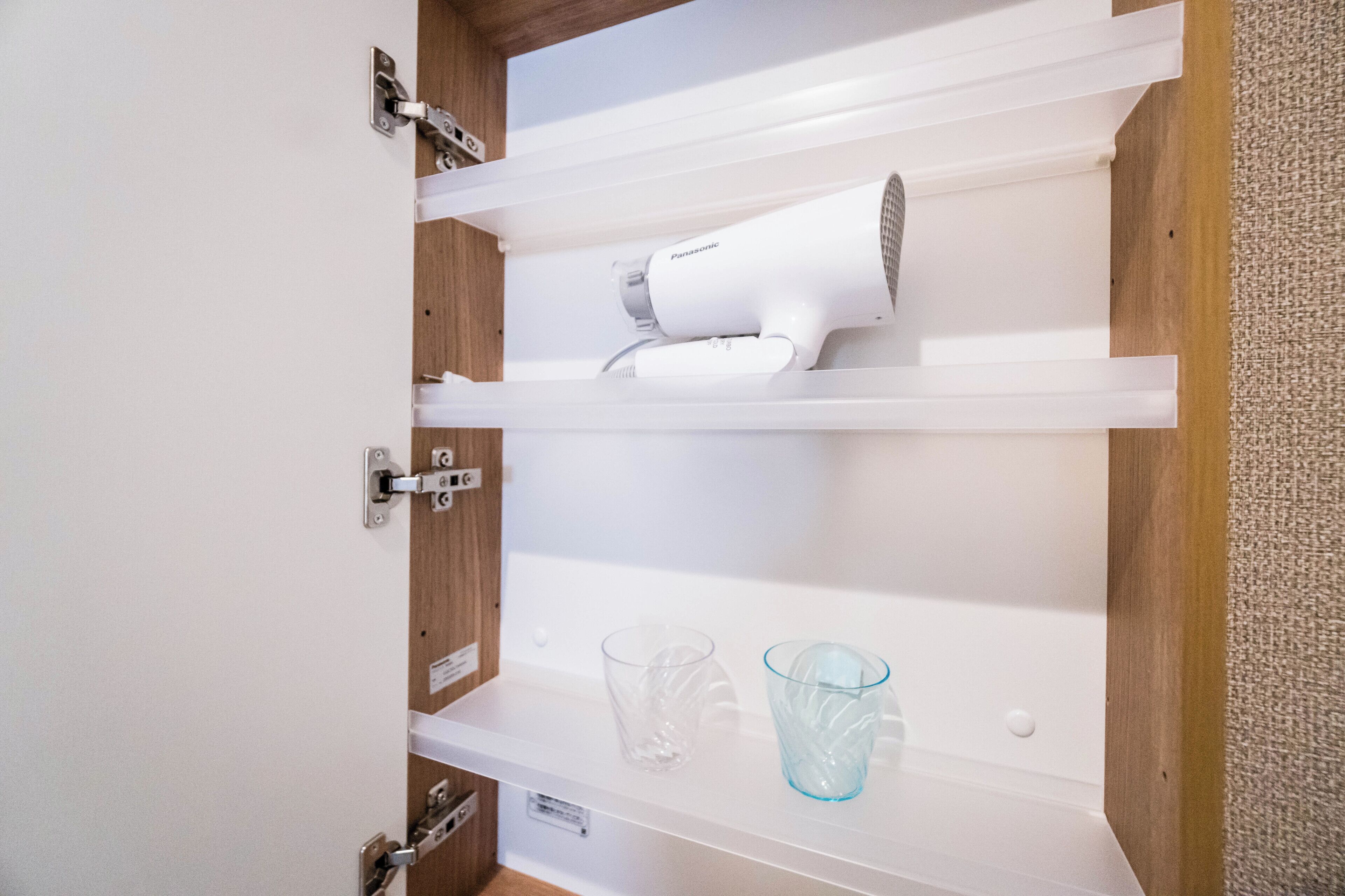 A bathroom with a white vanity, a hairdryer on the shelf, and two clear glasses on the counter.