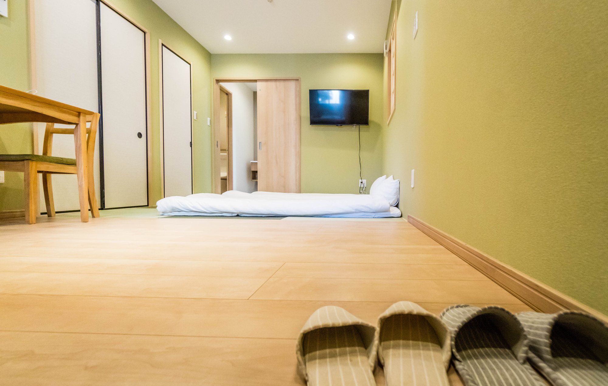 A hotel room with a bed, a TV mounted on the wall, a wooden floor, and a chair.