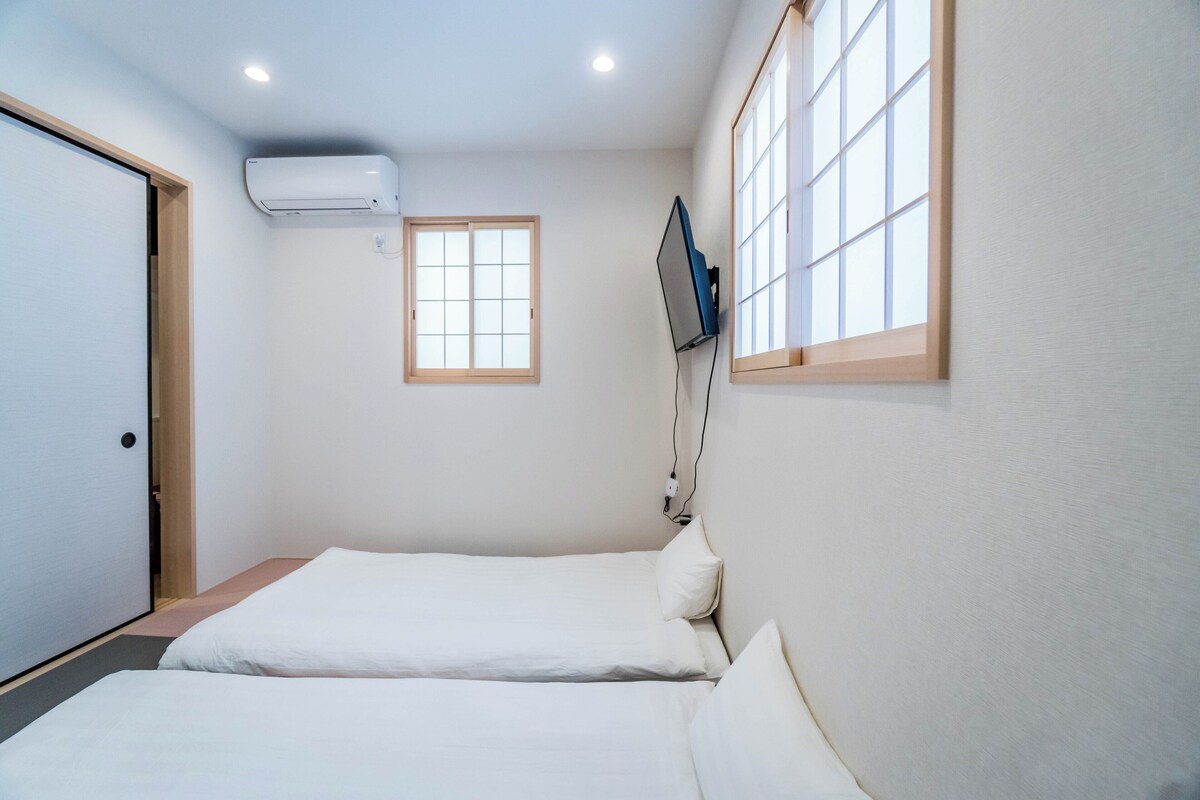 Ein Schlafzimmer mit zwei Betten, einem Fenster und einem am Wand montierten Fernseher.
