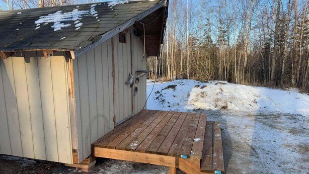 A small wooden shed with a metal roof, a wooden deck, and a snow-covered ground. - Alaska Native Steam Bath w/Power and Water for RV, free wifi (Wasilla)