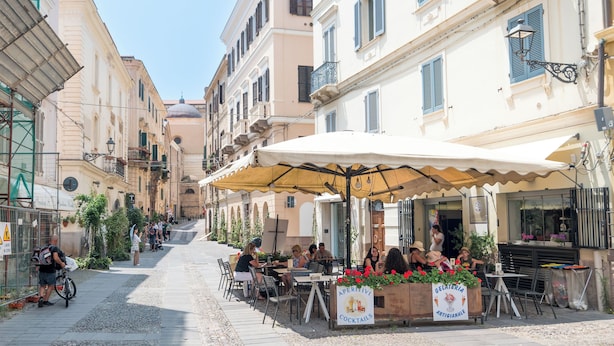 Una stretta via con tavolini all'aperto di fronte a una gelateria.
