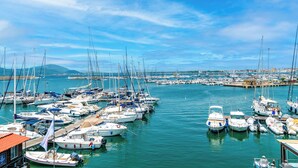 Una marina con numerose imbarcazioni ormeggiate, cielo sereno e una costa lontana con edifici.