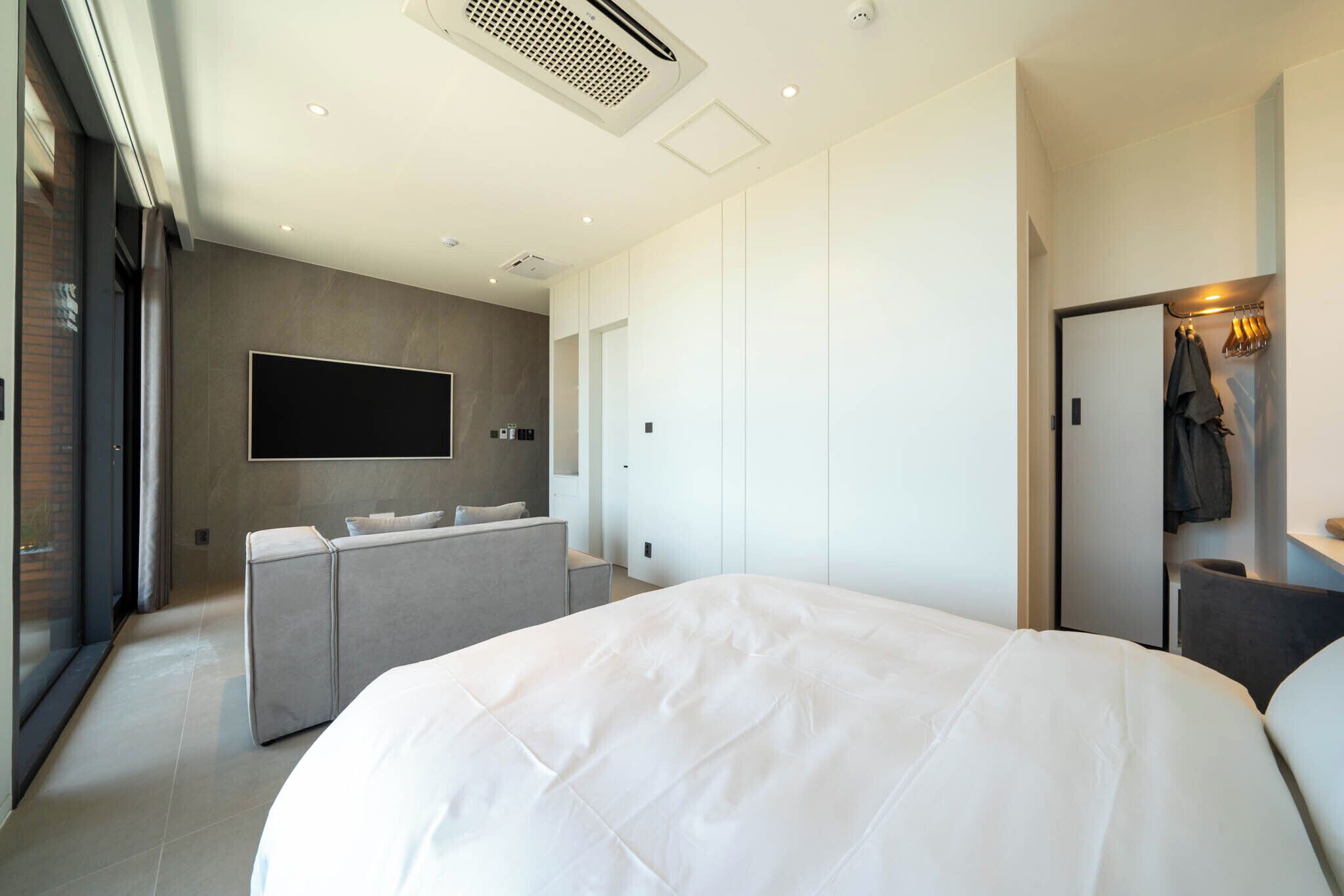 A modern hotel room with a large bed, a seating area, a flat-screen TV, and a wardrobe.