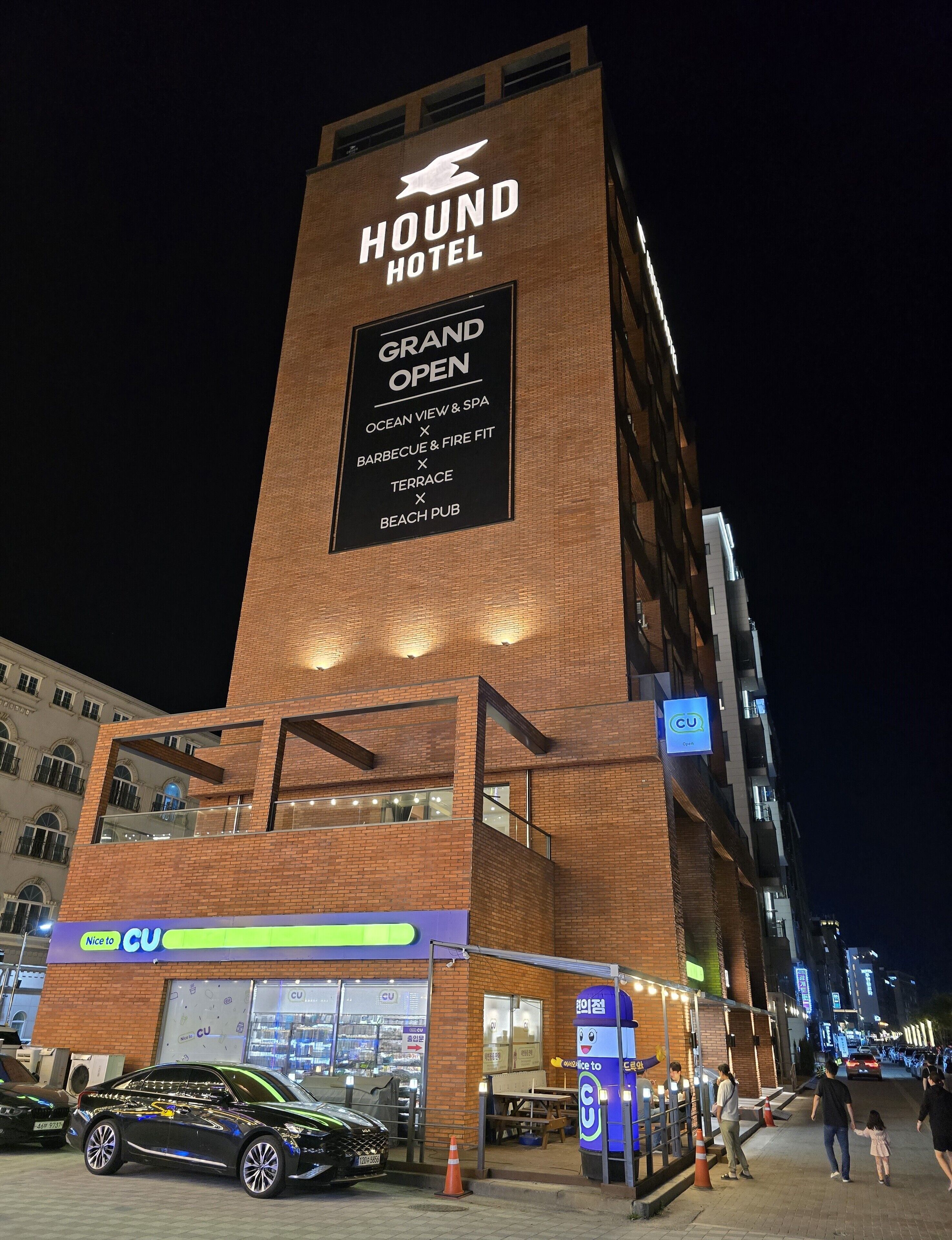 A hotel with a prominent sign indicating a grand opening, featuring amenities like an ocean view, barbecue, terrace, and beach pub.