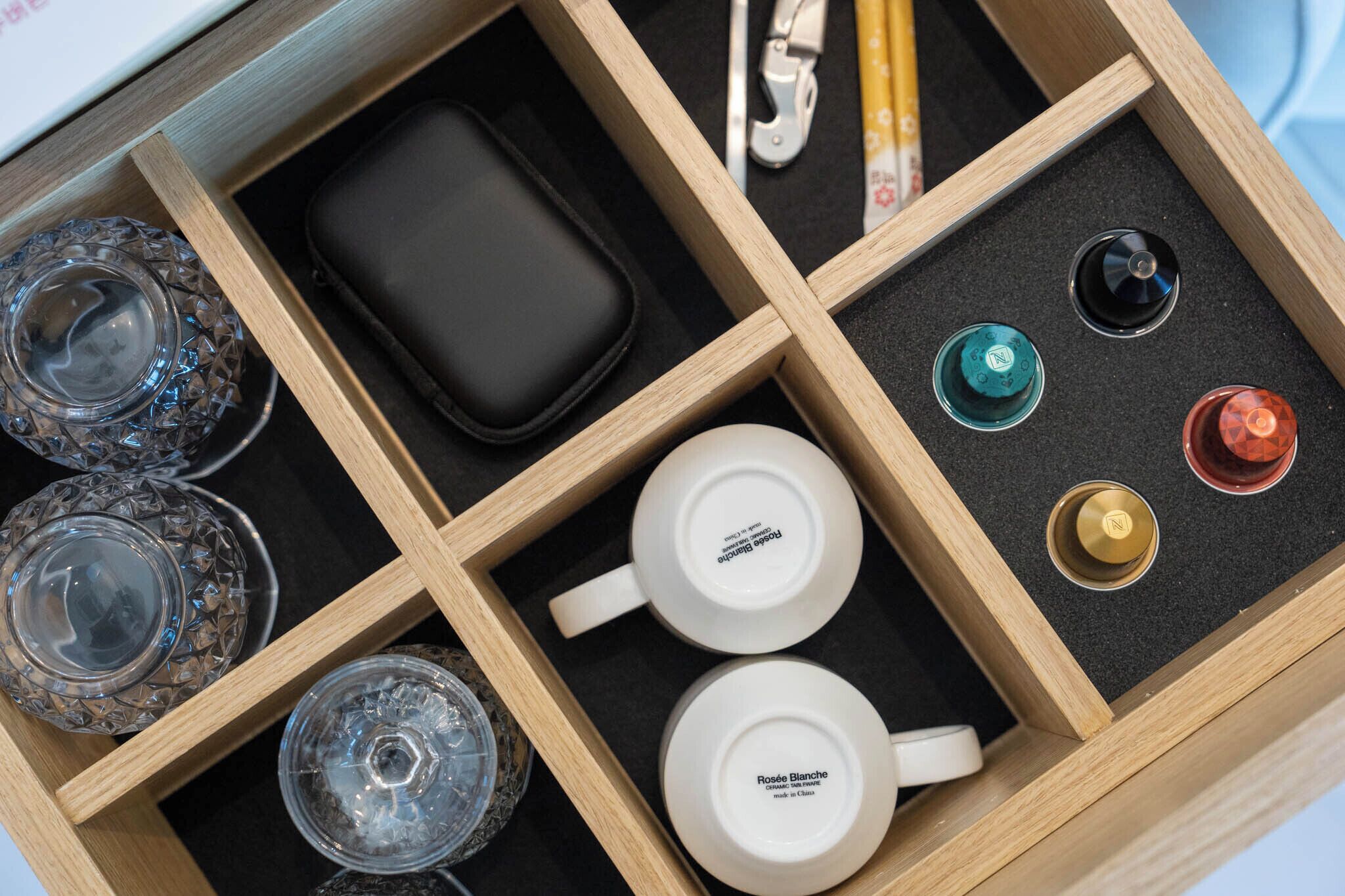 A wooden tray with compartments containing a black wallet, two white cups labeled "Rosée Blanche," and various other items.