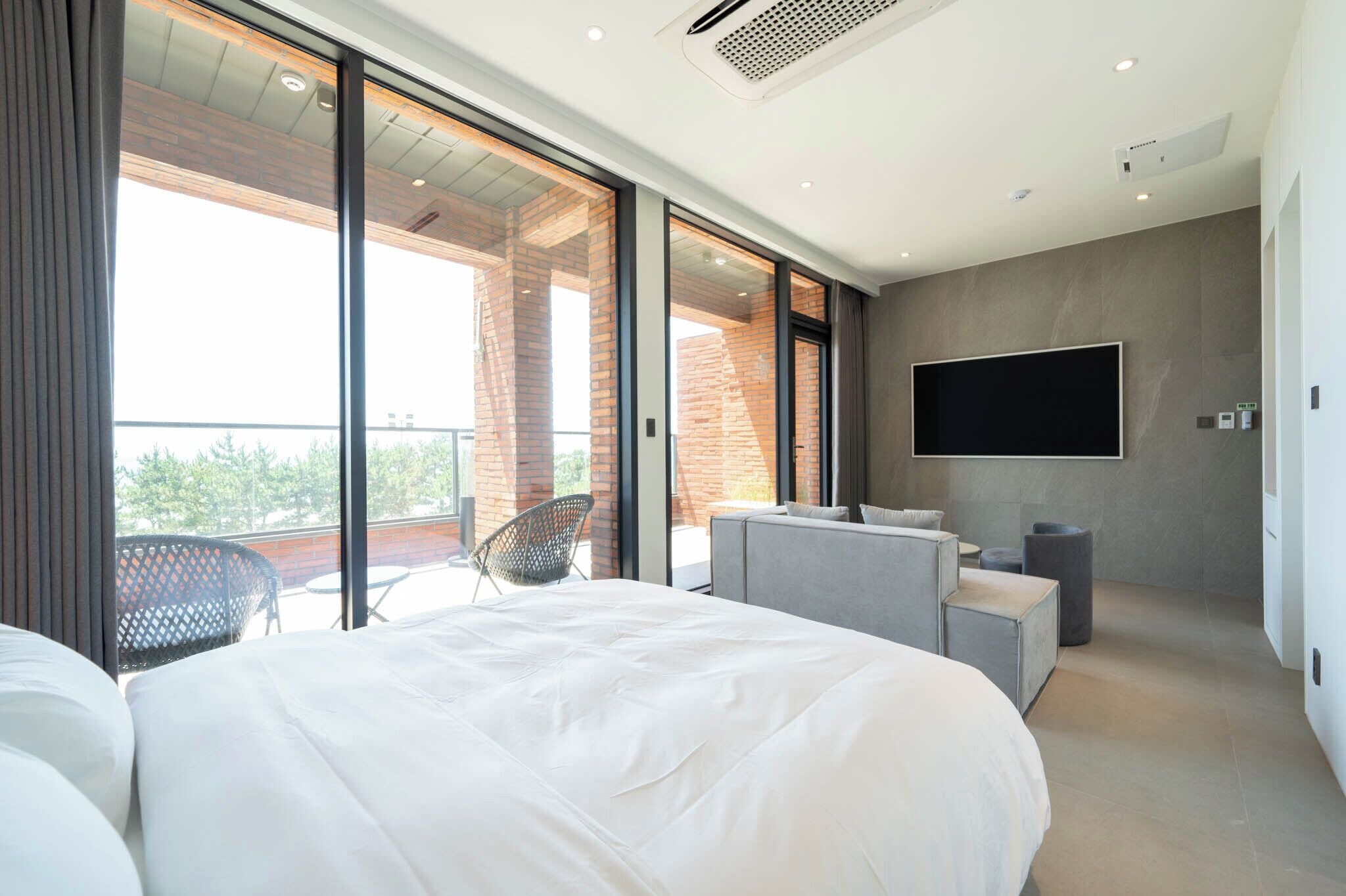 A modern bedroom with a large bed, a TV mounted on the wall, and a balcony with a chair.
