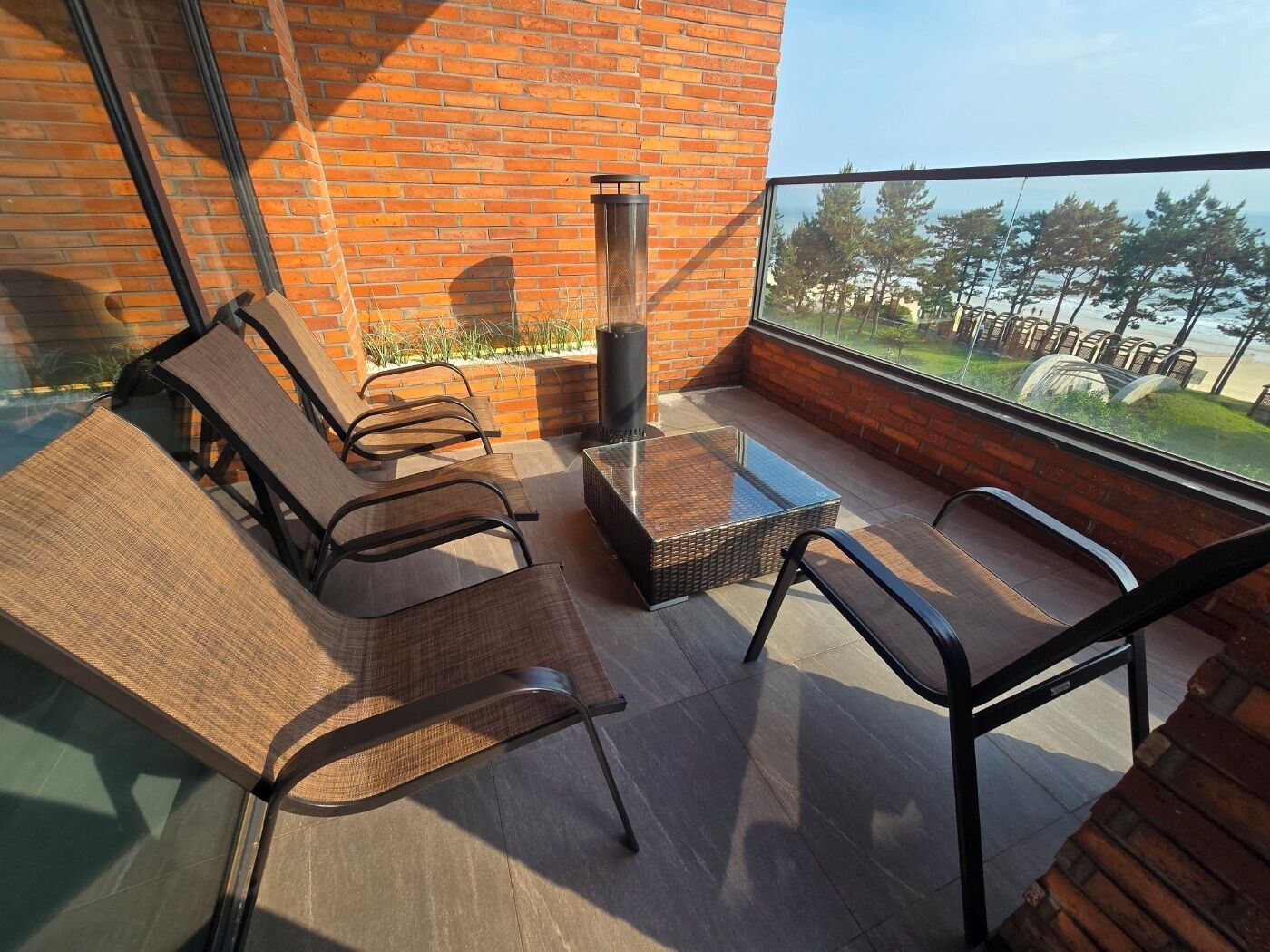 Un balcon avec une table en verre, deux chaises et un petit foyer.