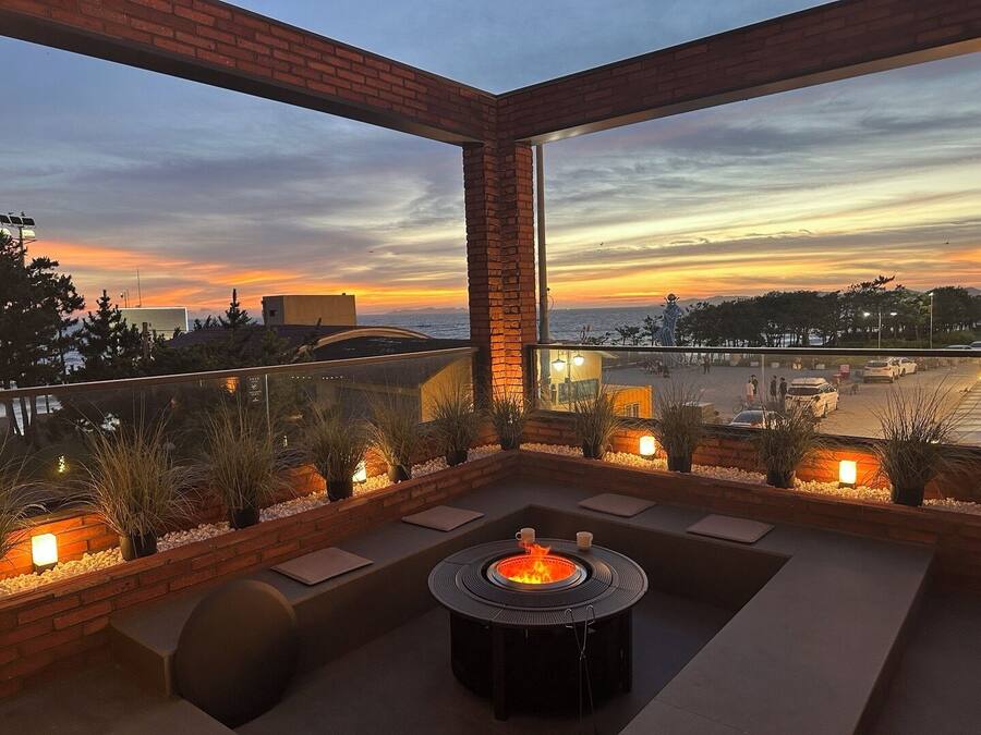Une terrasse sur le toit avec un foyer, des sièges et une vue sur le coucher de soleil sur l’océan.