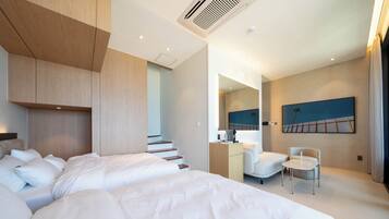 A modern hotel room with a large bed, a desk, a chair, and a staircase leading to an upper level.