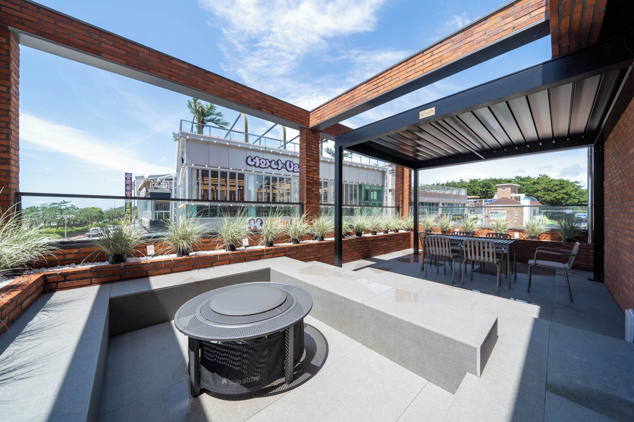 A rooftop patio with a round table and chairs, a brick wall, and a view of a building with a sign.