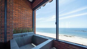 A modern bathroom with a large bathtub, a view of the beach, and a brick wall. - Hound Hotel Daecheon (Boryeong)