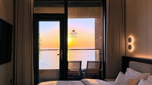 A hotel room with a bed, a desk, and a view of the sea at sunset. - Hound Hotel Daecheon (Boryeong)