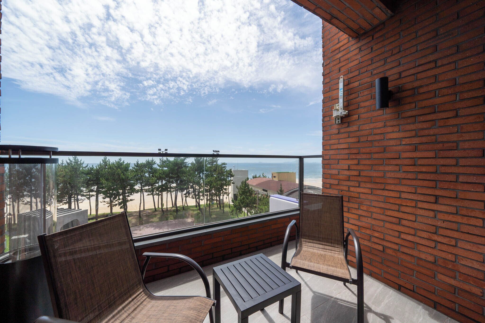 Un balcón con sillas de mimbre y una mesa, con vistas a una playa y un cielo despejado.