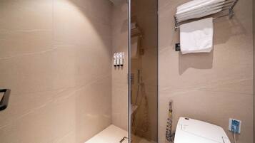 Un baño moderno con cabina de ducha de vidrio, un lavabo blanco y un perchero con toallas dobladas.