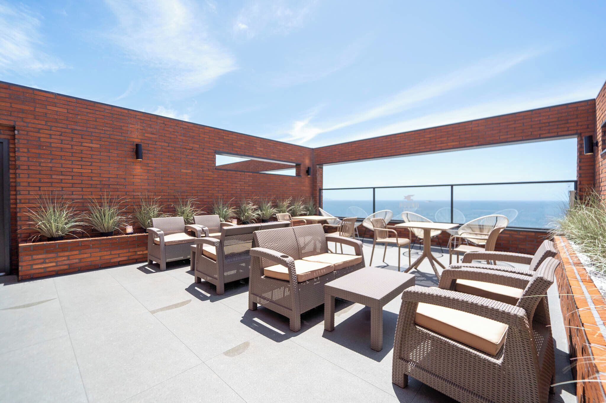 Una terraza en la azotea con mobiliario de mimbre, un muro de ladrillo y un ventanal con vistas al horizonte de la ciudad.
