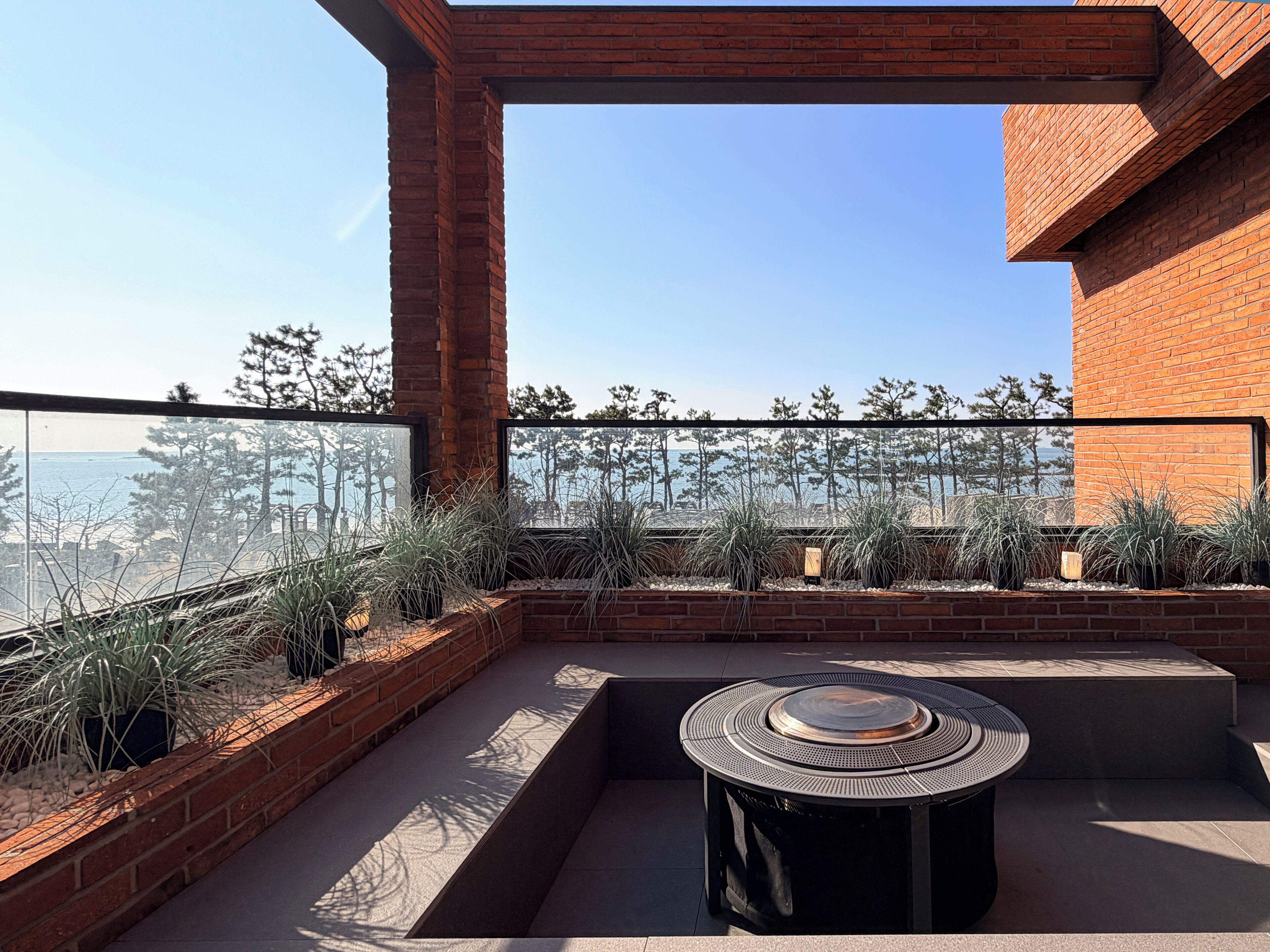 A rooftop patio with a round table, brick walls, and a view of the sea.