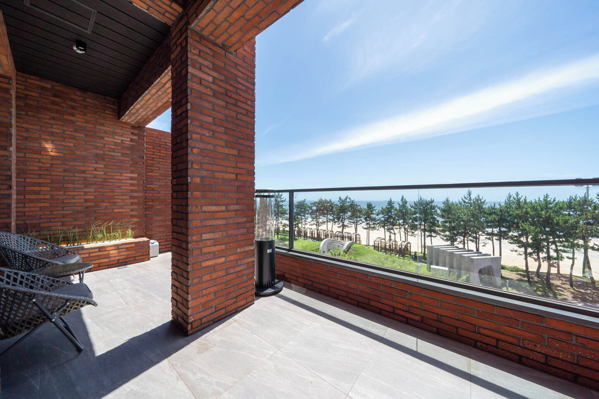 A balcony with a view of a beach and trees, featuring brick walls and a glass railing.