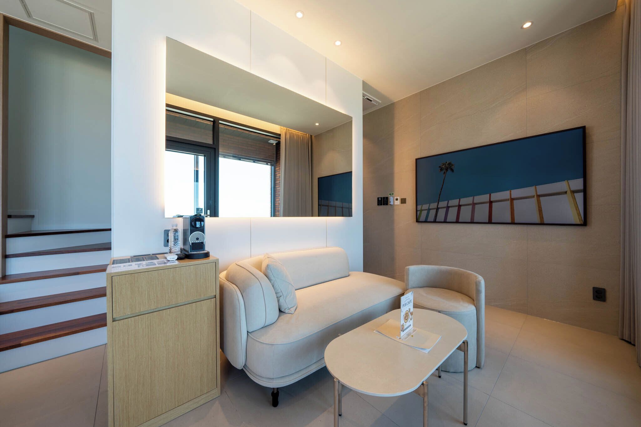Una habitación de hotel moderna con un sofá, una mesita, un armario y un cuadro en la pared.