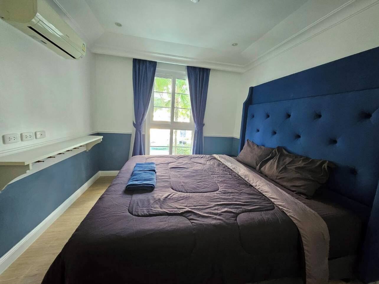 A bedroom with a bed, a blue headboard, and a window with curtains.
