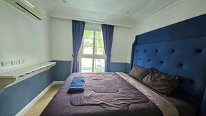 A bedroom with a bed, a blue headboard, and a window with curtains.