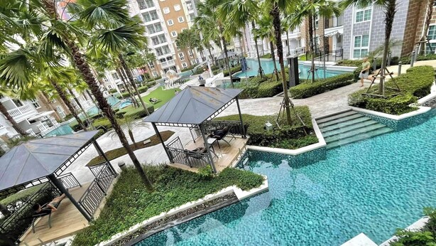 A resort with a large pool, palm trees, and a covered seating area.