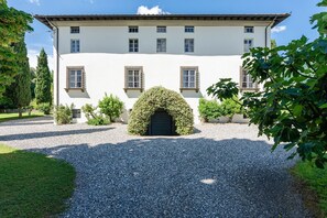 Stately building with a central entrance, flanked by two windows, set amidst lush greenery and a neatly trimmed hedge.