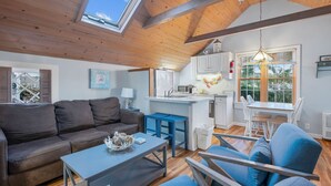 Un salon chaleureux avec un canapé, une table basse et des fauteuils bleus. Il y a également un coin cuisine avec des placards blancs et une table à manger.