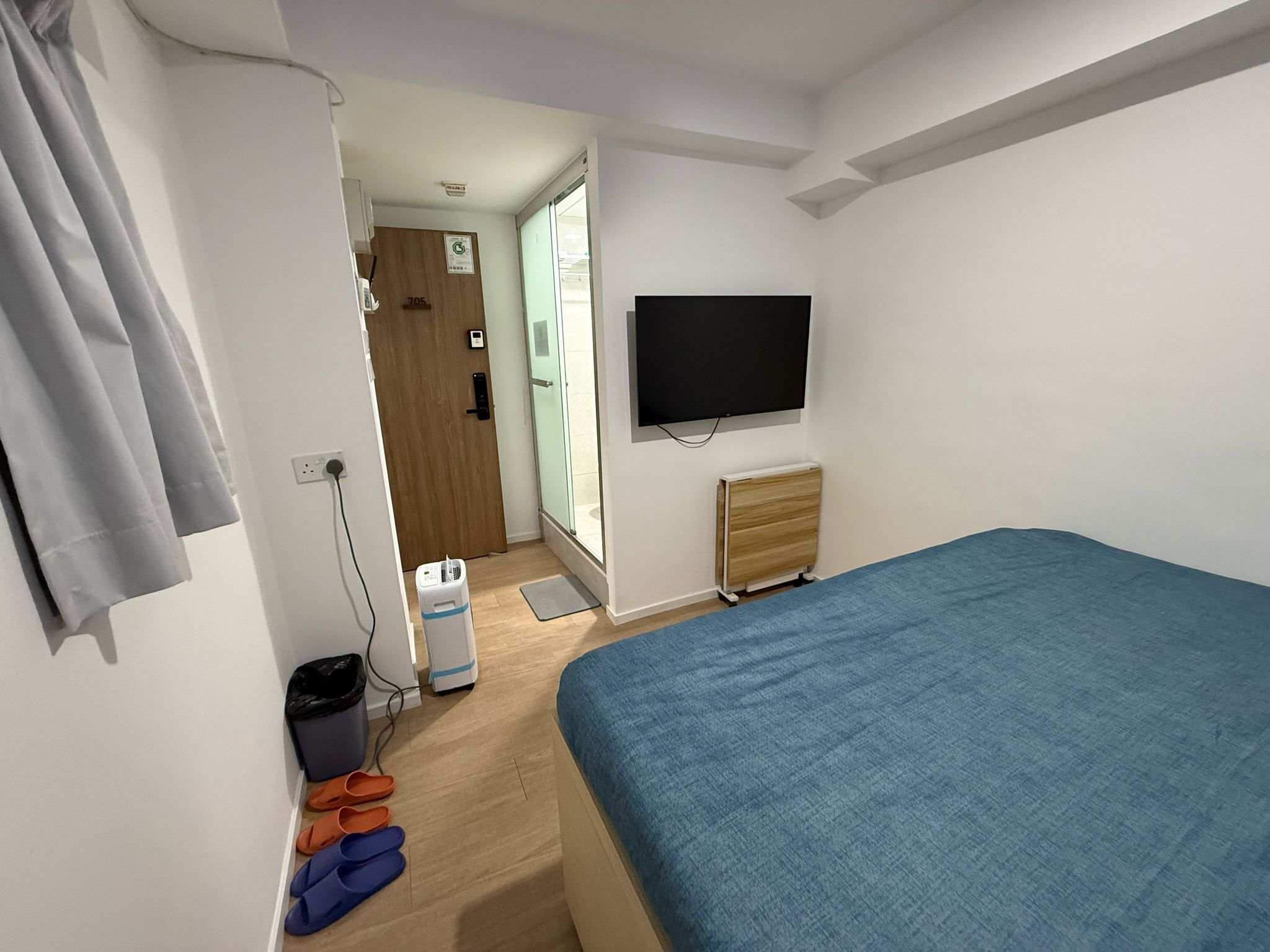 A bedroom with a bed, a TV, a radiator, a door, and a window.