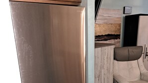 Una cocina con un refrigerador de acero inoxidable, armarios de madera, una silla blanca y piso de madera.