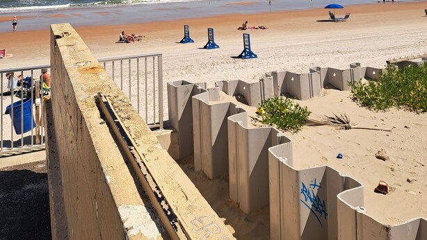 Una playa con un muro de hormigón, algunas sillas de playa y un cielo azul despejado.