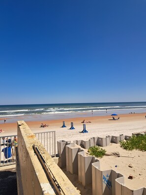 Ein Strand mit einer Betonbarriere, einigen Liegestühlen und einem wolkenlosen, blauen Himmel.
