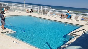 Una piscina azul cristalina con indicador de profundidad de 1.4 metros, rodeada por una valla blanca y sillas de descanso.