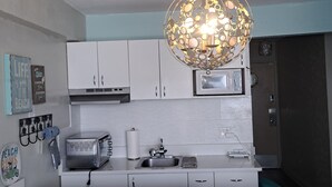 Una cocina moderna con armarios blancos, un refrigerador de acero inoxidable, un microondas y una lámpara colgante esférica original.