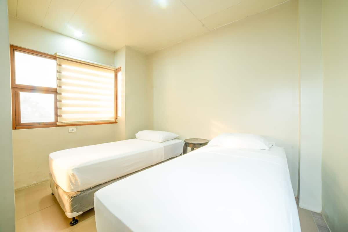 A room with two single beds, a small round table, and a window with blinds.