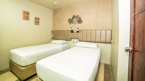 Una camera d'albergo con due letti singoli, un poggiatesta in legno e un punto luce a parete.