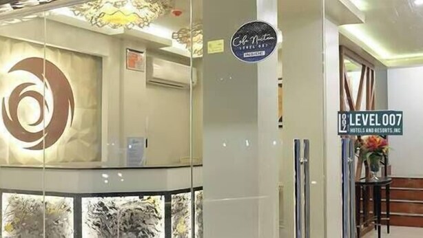 Un'area reception di un hotel dal design moderno, con un ampio logo circolare a parete, una scrivania della reception e una segnaletica che indica il nome e il piano dell'hotel.
