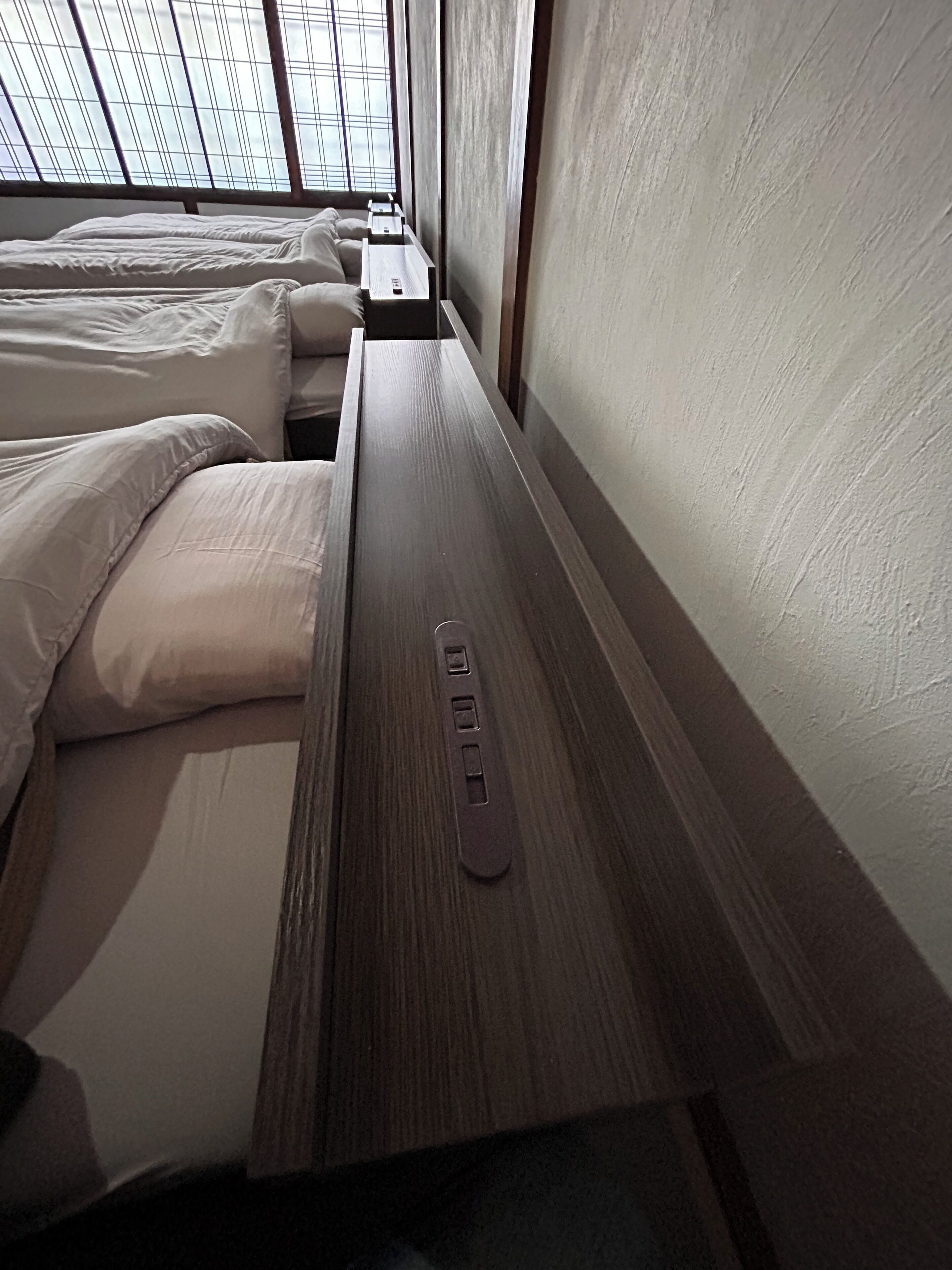 Een kamer met twee bedden, een houten bankje en een raam met een rasterpatroon.