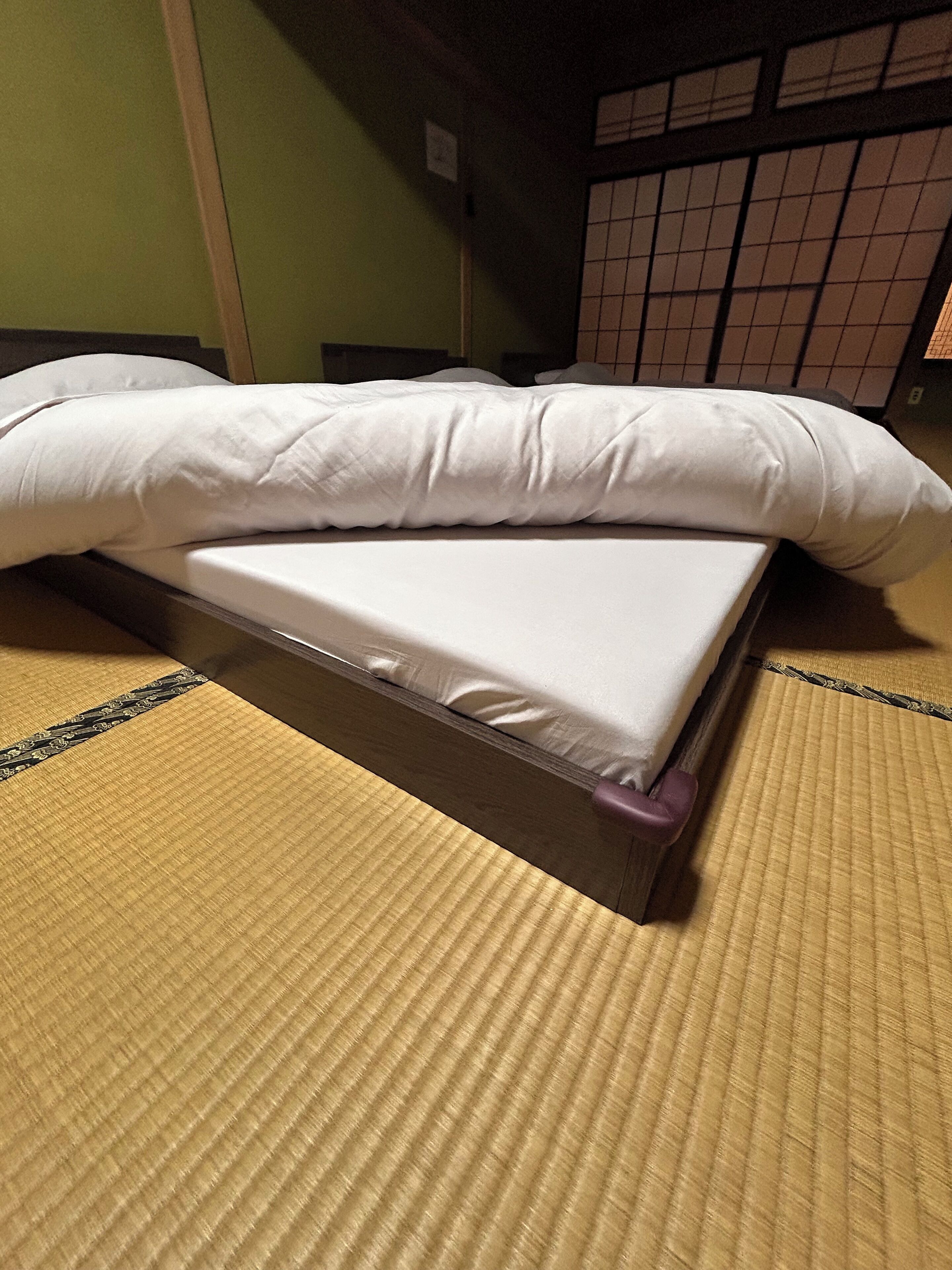 A bed with a white mattress and pillows, placed on tatami flooring.