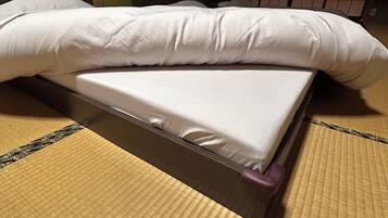Una cama con colchón y almohadas blancas sobre suelo de tatami.