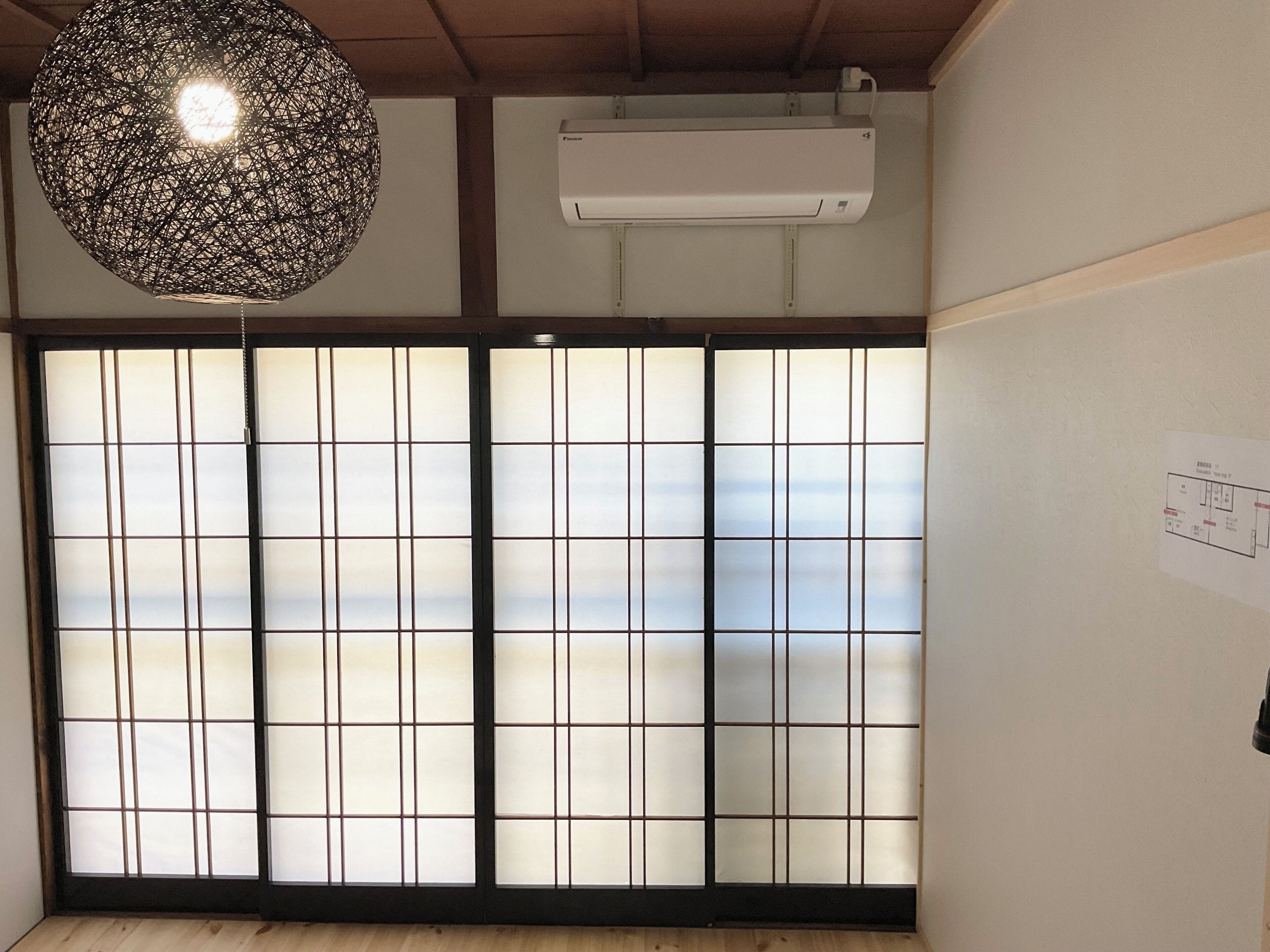 A room with a large shoji screen door, a hanging light fixture, and an air conditioning unit.